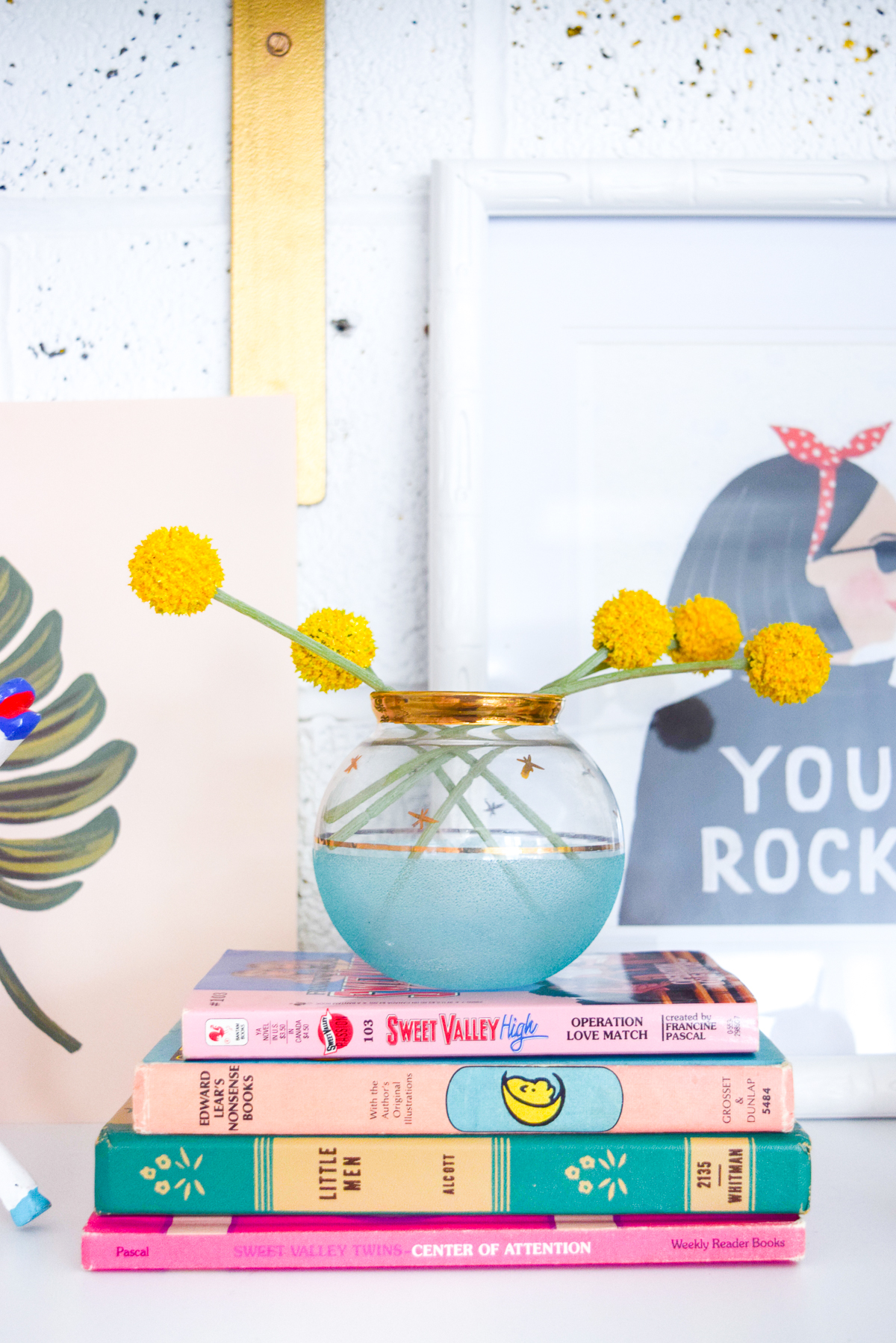 Who would have thought that gold shelf brackets would have kicked-off a pink & gold office revamp? Full of bright colours, gold, playful touches and accessories from women owned stores, what's not to love?s stack of pink and blue books with billy buttons on top