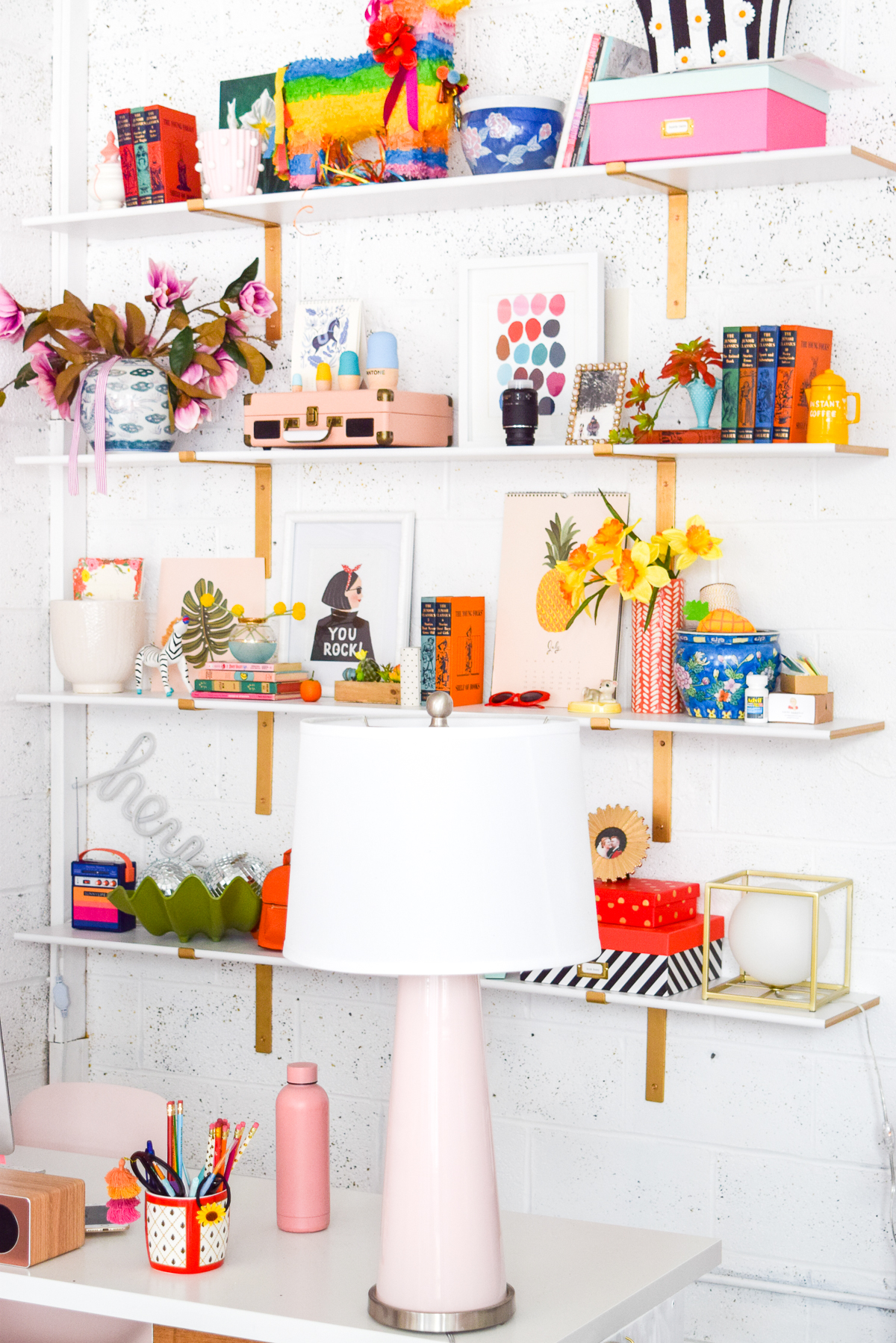 Who would have thought that gold shelf brackets would have kicked-off a pink & gold office revamp? Full of bright colours, gold, playful touches and accessories from women owned stores, what's not to love? Pink lamp in front of office bookshelves