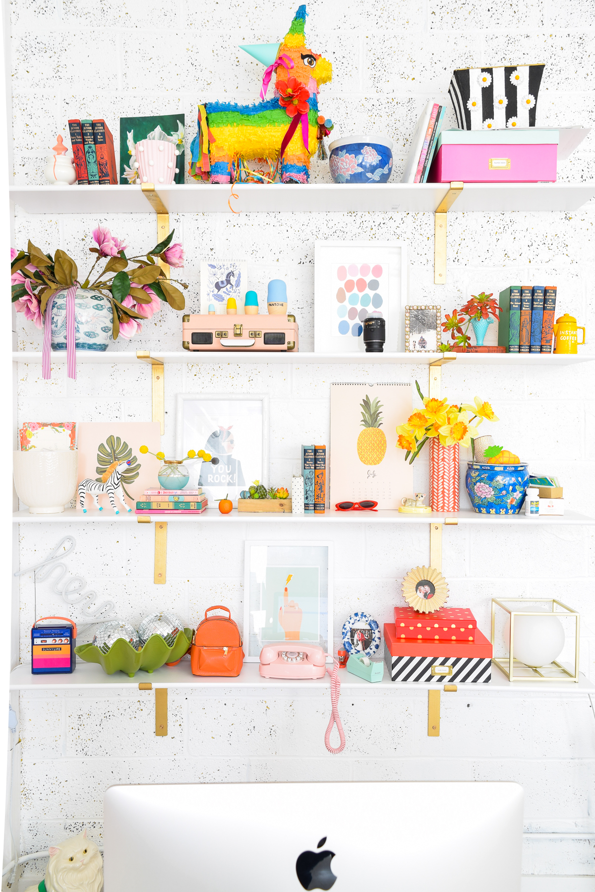 Who would have thought that gold shelf brackets would have kicked-off a pink & gold office revamp? Full of bright colours, gold, playful touches and accessories from women owned stores, what's not to love? colourfully decorated shelves behind a mac desktop