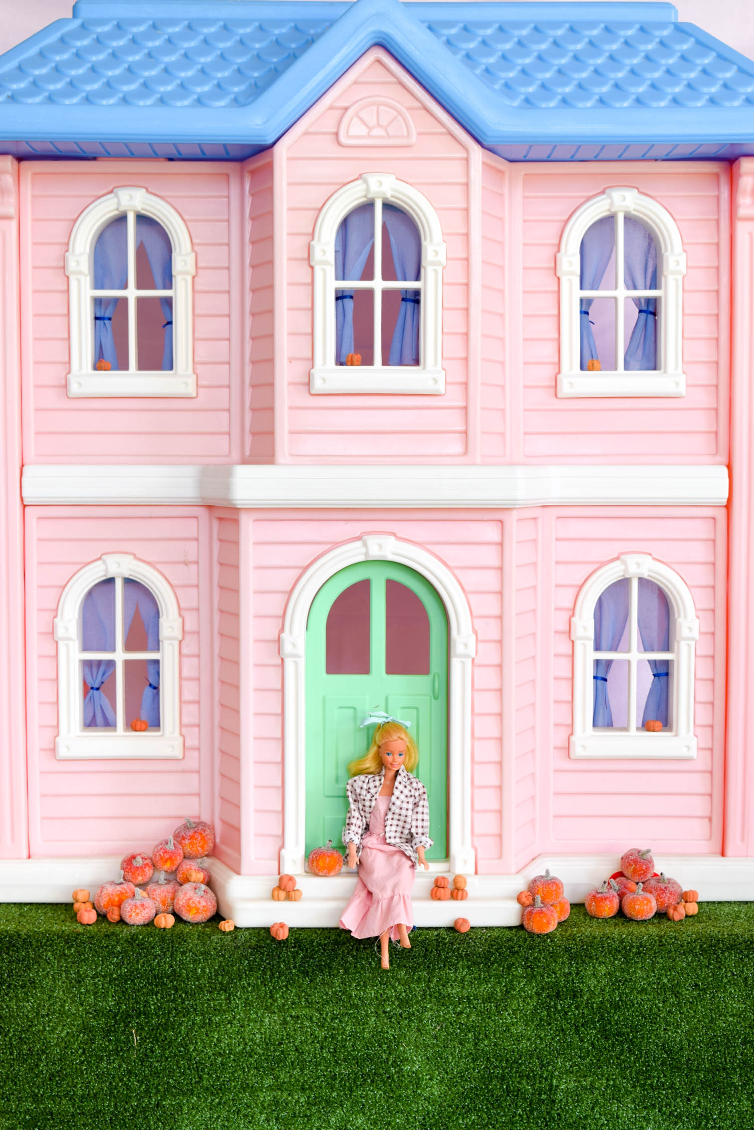 Barbie sitting on front step of large dream house with pumpkins o either side