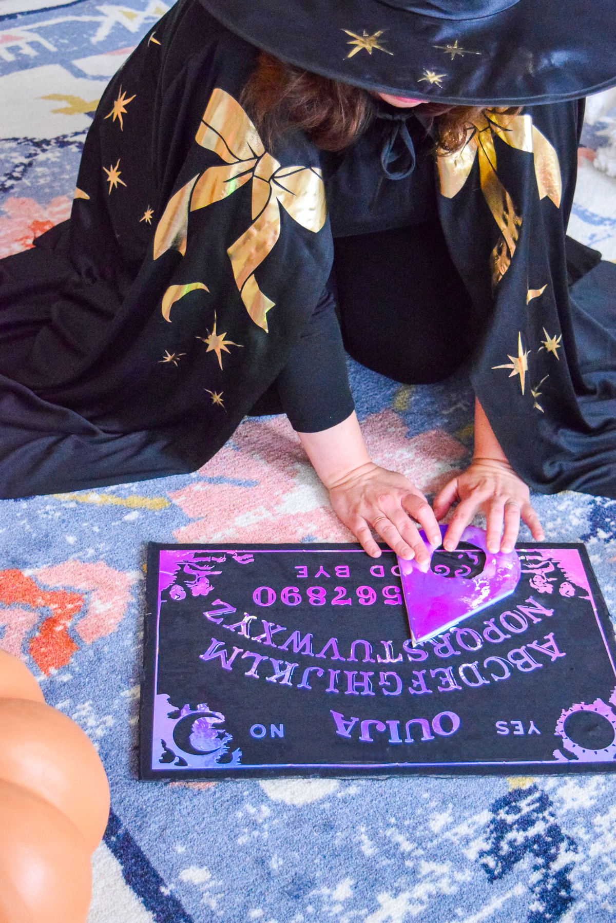 woman in a witch cape moving a planchette on a holographic ouija board