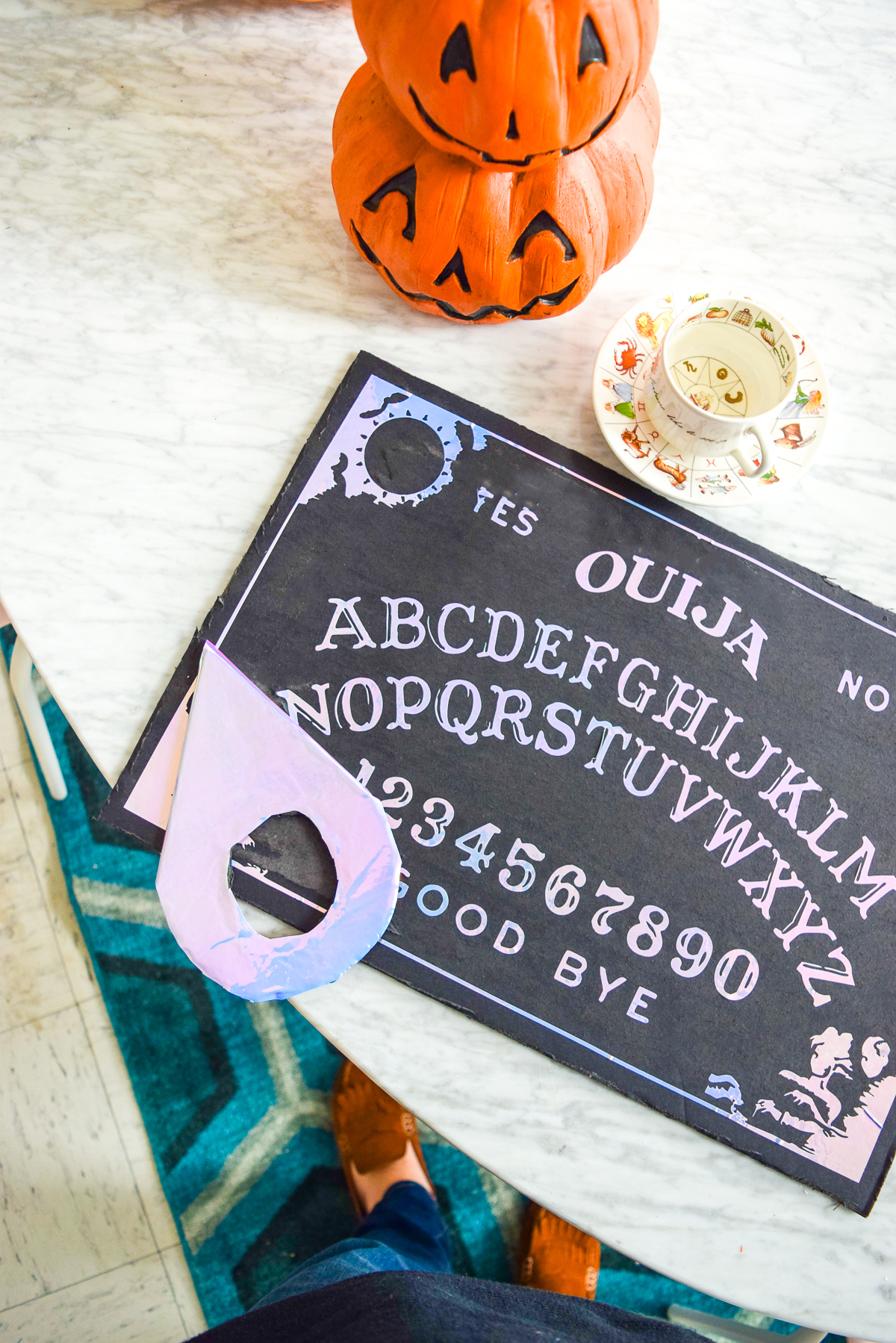 holographic ouija board sitting on a marble table with stacked pumpkins